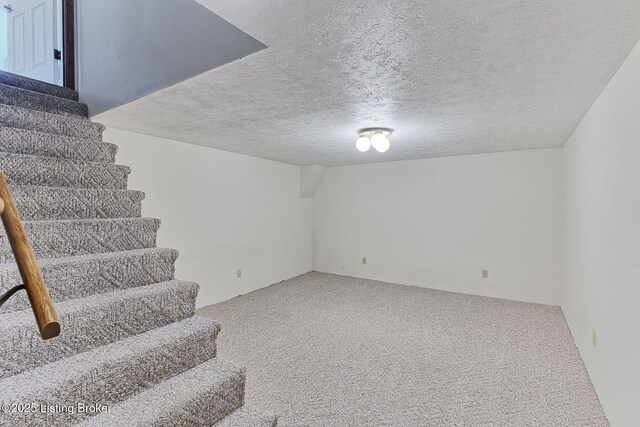 finished basement with a textured ceiling, stairway, and carpet