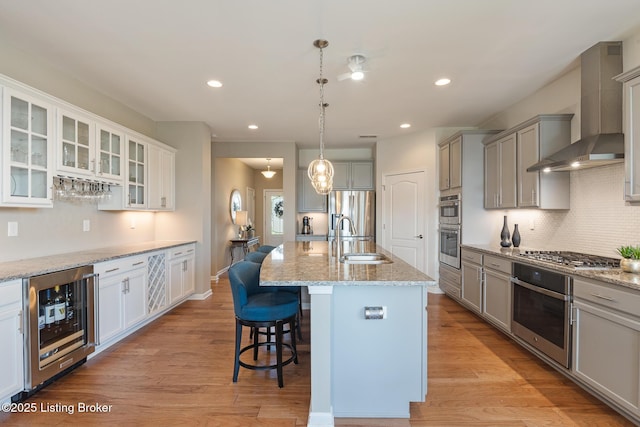 kitchen with wall chimney range hood, tasteful backsplash, light stone countertops, a sink, and beverage cooler