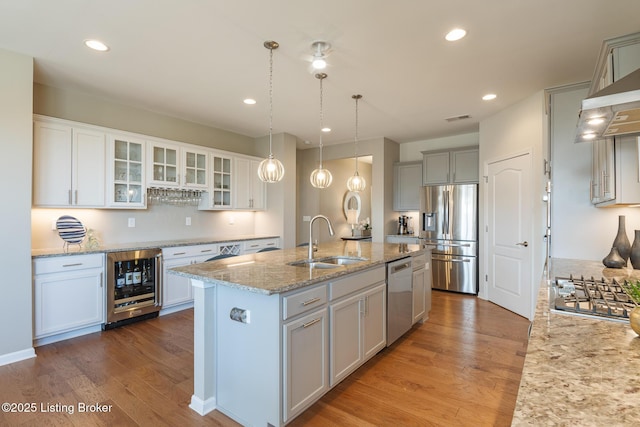 kitchen featuring light stone countertops, a sink, stainless steel appliances, wine cooler, and a center island with sink