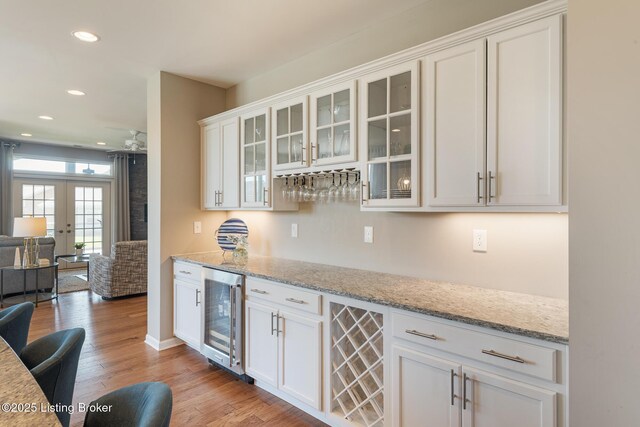 bar with french doors, recessed lighting, light wood-type flooring, wine cooler, and a bar