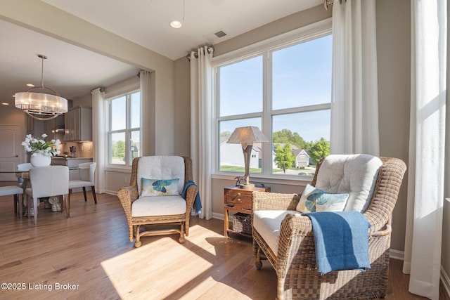 living area with an inviting chandelier, baseboards, light wood-style floors, and visible vents