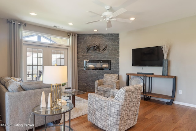 living area featuring ceiling fan, a fireplace, wood finished floors, and visible vents