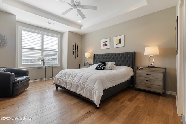 bedroom with visible vents, baseboards, a raised ceiling, and wood finished floors