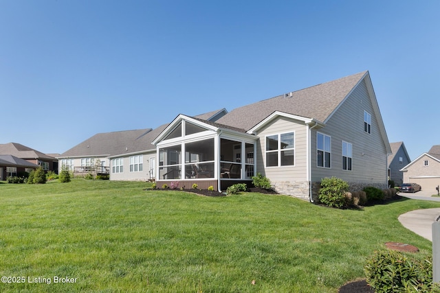 rear view of house featuring a lawn, stone siding, and a sunroom