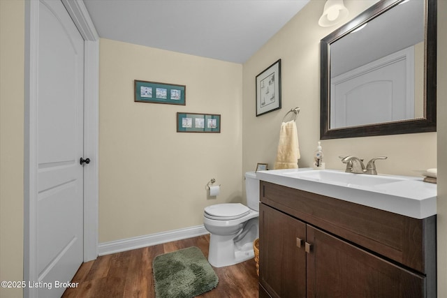 half bathroom featuring baseboards, wood finished floors, toilet, and vanity