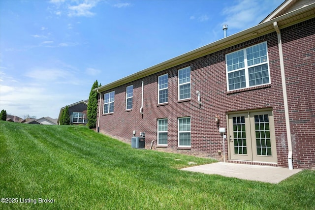 back of house with central air condition unit, brick siding, and a yard