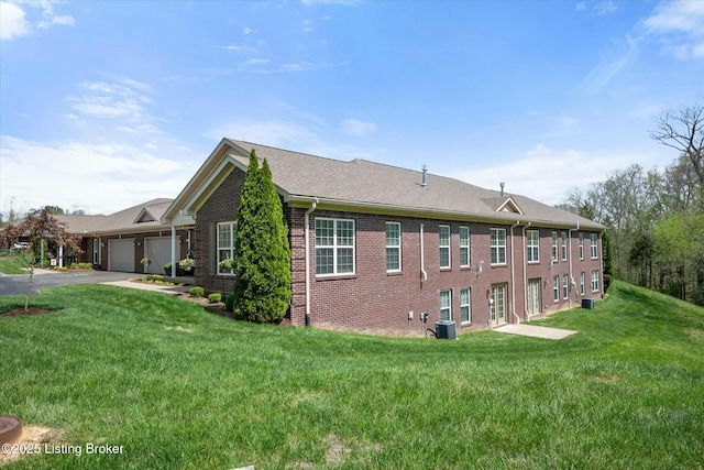 view of property exterior featuring aphalt driveway, central air condition unit, an attached garage, a lawn, and brick siding