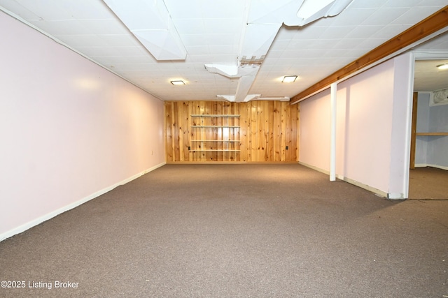finished below grade area featuring wooden walls, carpet floors, baseboards, and a paneled ceiling