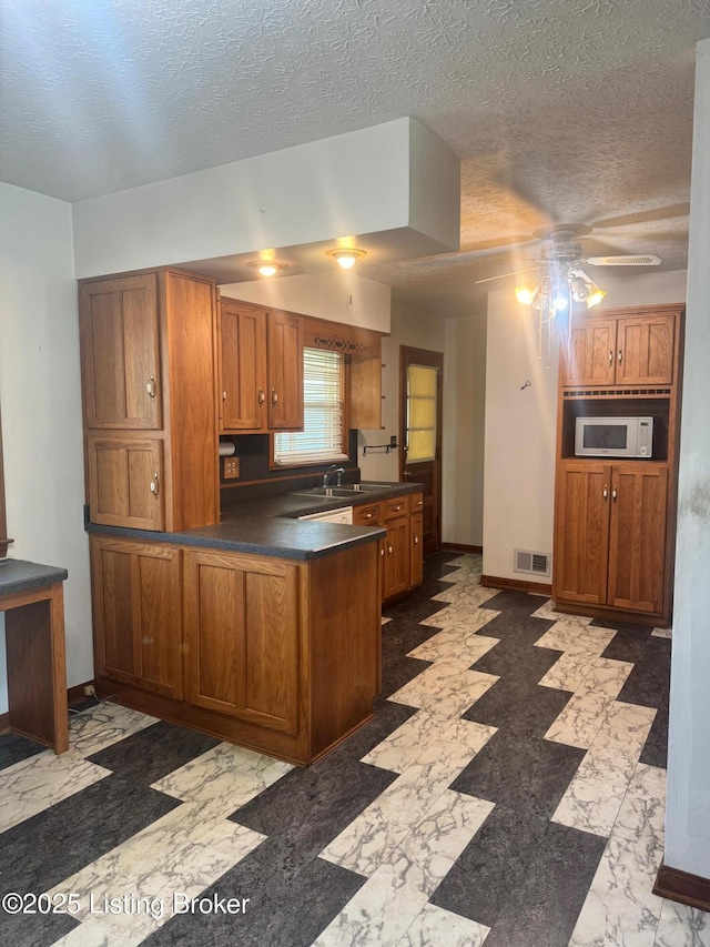 kitchen with visible vents, a peninsula, white microwave, a textured ceiling, and brown cabinets