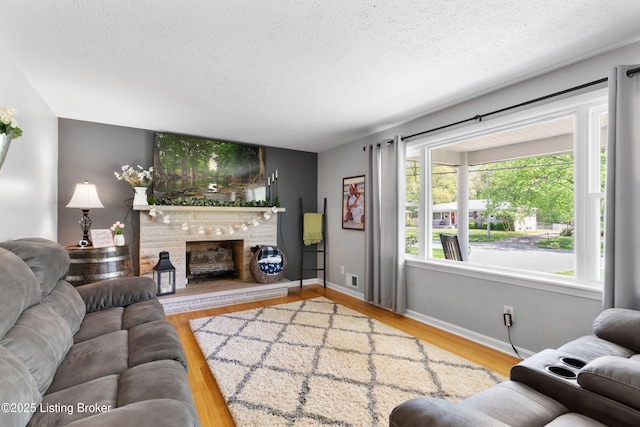 living area with baseboards, wood finished floors, a textured ceiling, and a fireplace