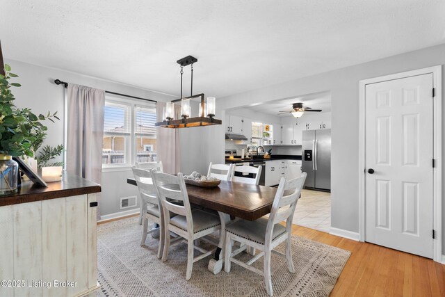 dining area with baseboards, a ceiling fan, light wood finished floors, and visible vents