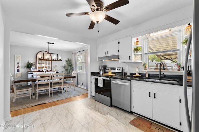 kitchen featuring a sink, dark countertops, white cabinetry, under cabinet range hood, and appliances with stainless steel finishes