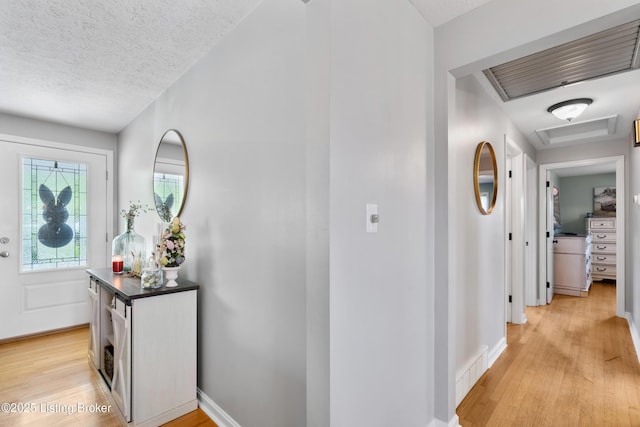 foyer entrance with a textured ceiling, light wood finished floors, and visible vents