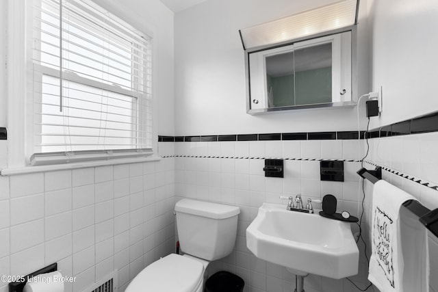 bathroom with tile walls, a wainscoted wall, a sink, and toilet