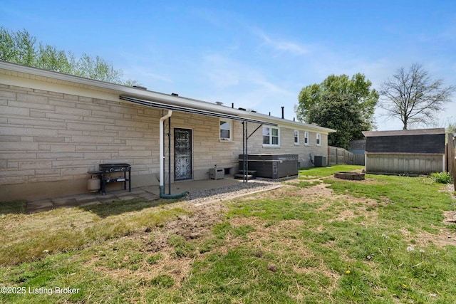 back of house with a fenced backyard, a storage shed, an outbuilding, stone siding, and a lawn