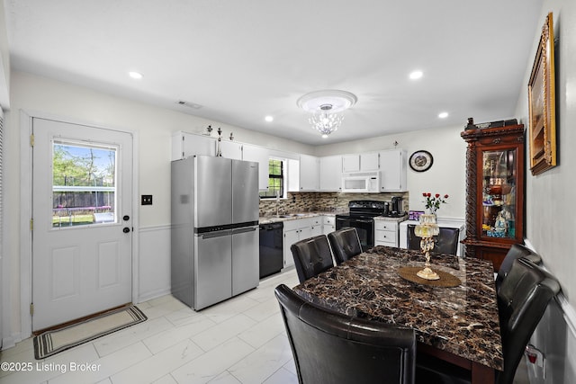 kitchen with black appliances, decorative backsplash, white cabinetry, and visible vents