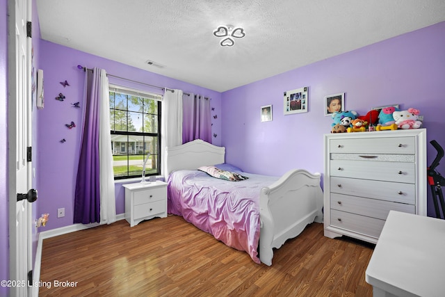 bedroom with a textured ceiling, wood finished floors, visible vents, and baseboards