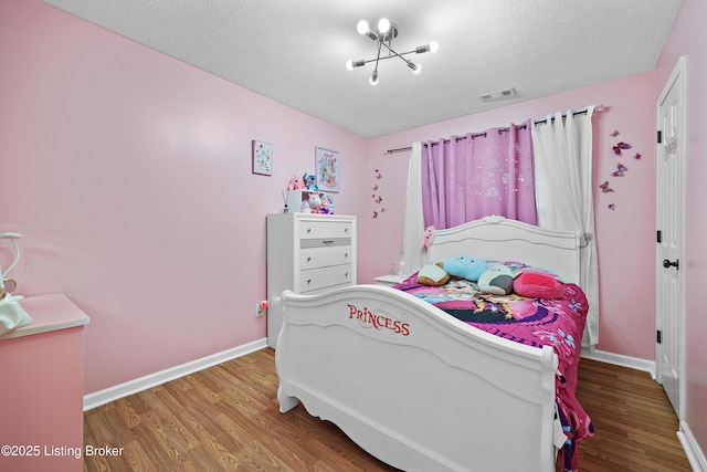 bedroom featuring baseboards, wood finished floors, visible vents, and a textured ceiling