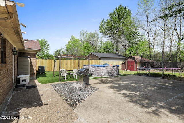 view of patio with a storage shed, a fenced backyard, a grill, central AC, and a trampoline