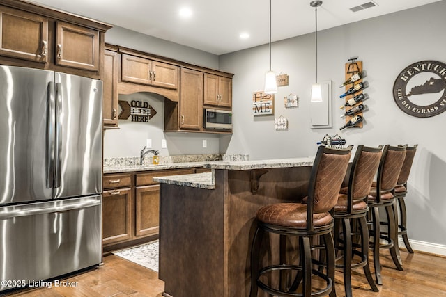 10905 Rock Valley Ct, Louisville, KY 40241 - kitchen with stainless steel appliances, wood finished floors, a kitchen breakfast bar, light stone countertops, and hanging light fixtures