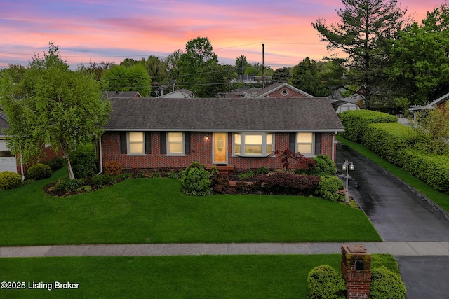 view of front of property with roof with shingles, a yard, and brick siding