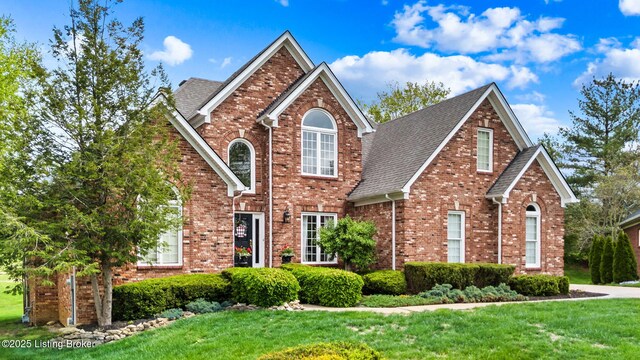 traditional-style house with brick siding, roof with shingles, and a front lawn