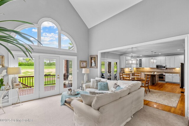 living area with light wood-type flooring, french doors, high vaulted ceiling, and a notable chandelier