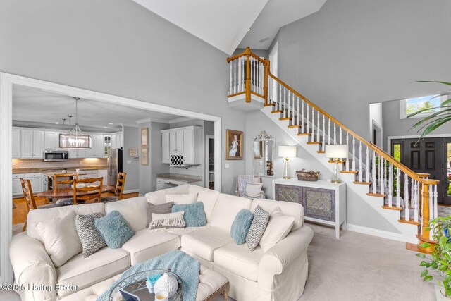 living room featuring high vaulted ceiling, a notable chandelier, stairs, and light colored carpet