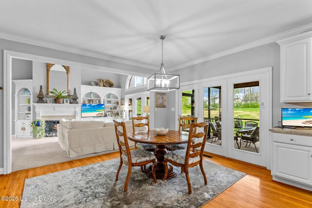 dining space with an inviting chandelier, a high end fireplace, ornamental molding, french doors, and light wood-style flooring