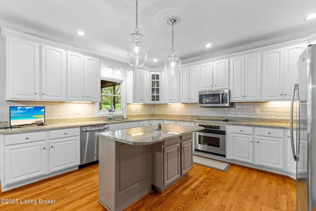 kitchen featuring white cabinets, a sink, light wood-type flooring, hanging light fixtures, and appliances with stainless steel finishes