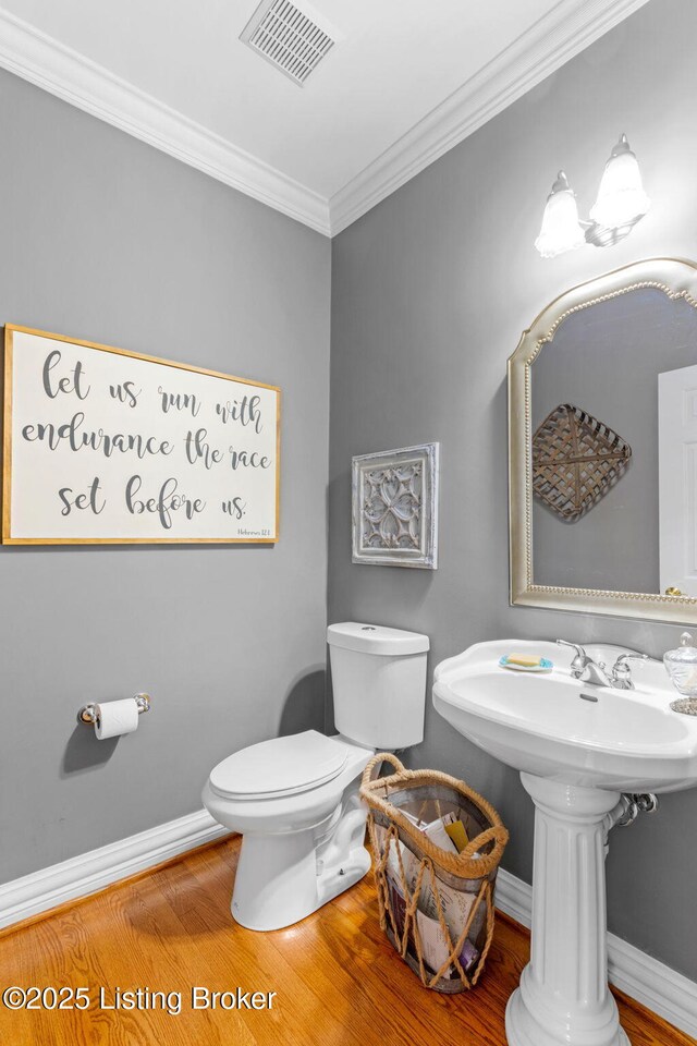 half bath with toilet, visible vents, baseboards, wood finished floors, and crown molding