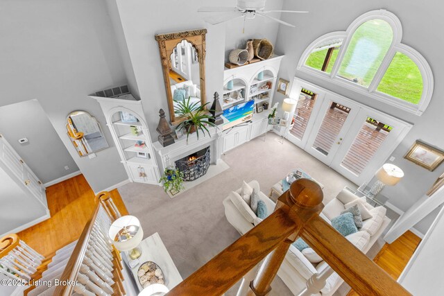 living area featuring baseboards, a towering ceiling, a premium fireplace, wood finished floors, and ceiling fan