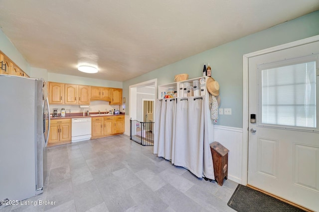 kitchen with light brown cabinets, light countertops, white dishwasher, freestanding refrigerator, and wainscoting