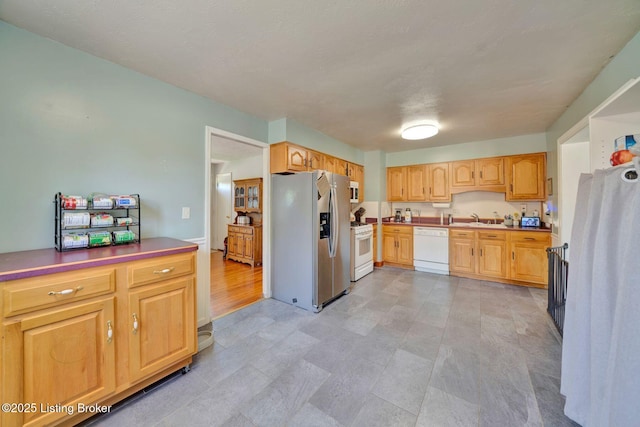 kitchen featuring light brown cabinetry, a sink, and white appliances