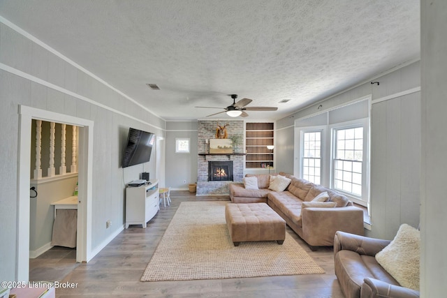 living room featuring built in shelves, ceiling fan, a brick fireplace, and plenty of natural light