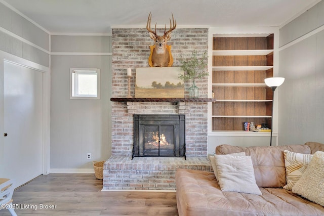 living area with baseboards, wood finished floors, ornamental molding, and a fireplace