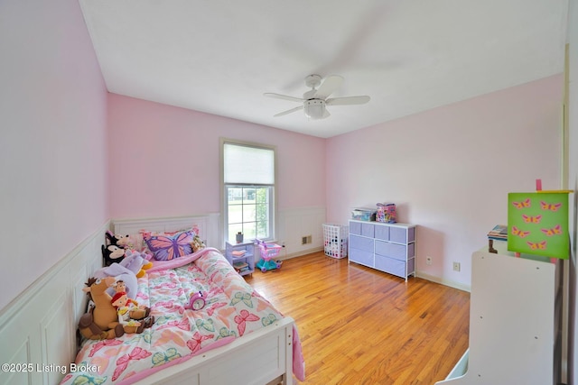 bedroom with light wood-style floors, a ceiling fan, visible vents, a decorative wall, and wainscoting