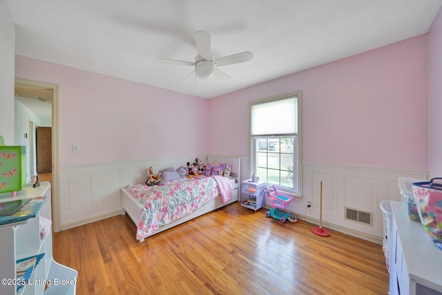 bedroom with visible vents, wainscoting, light wood-style floors, and ceiling fan