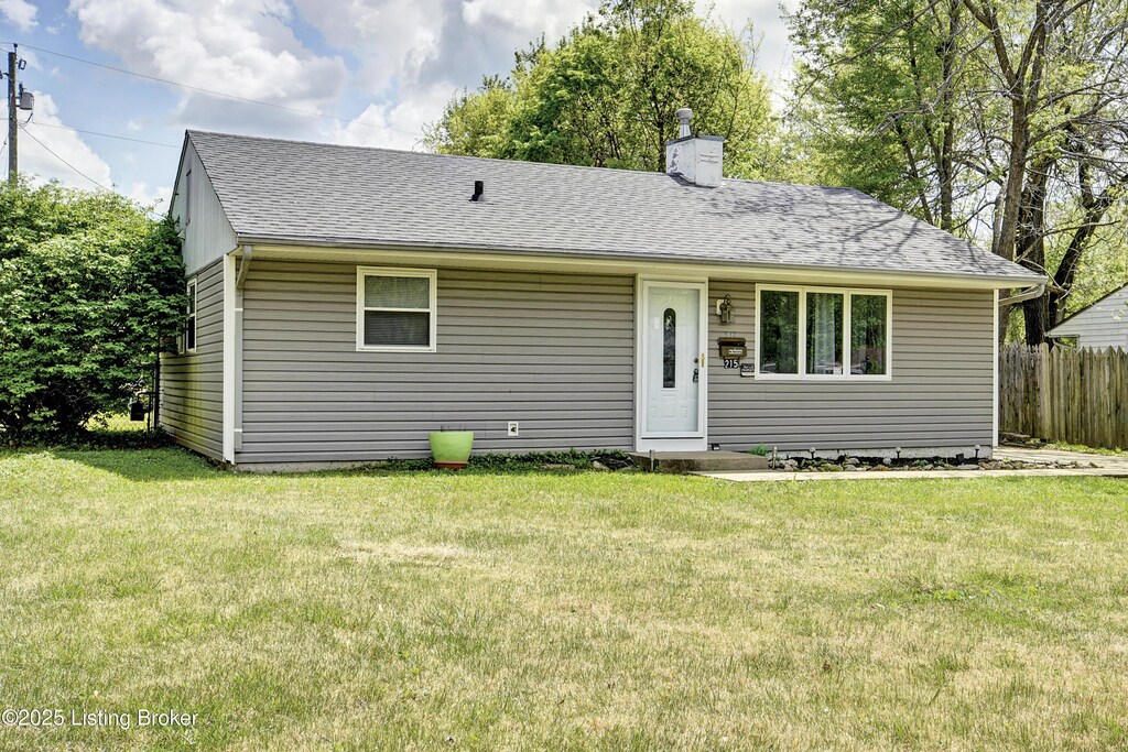 view of front of home with fence, a chimney, a front yard, and a shingled roof