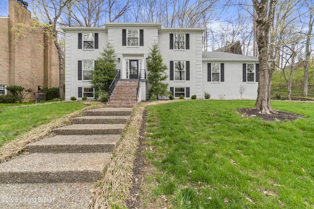 colonial house featuring brick siding, a front yard, and central AC unit