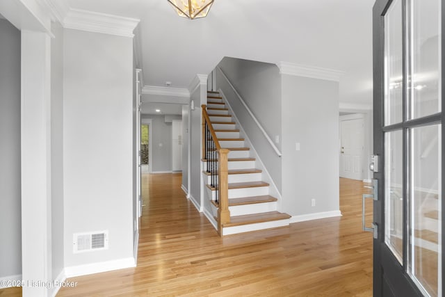 entrance foyer with light wood-style flooring, baseboards, visible vents, stairway, and ornamental molding