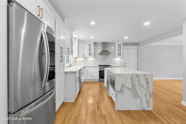 kitchen with white cabinetry, backsplash, wall chimney range hood, a kitchen island, and appliances with stainless steel finishes