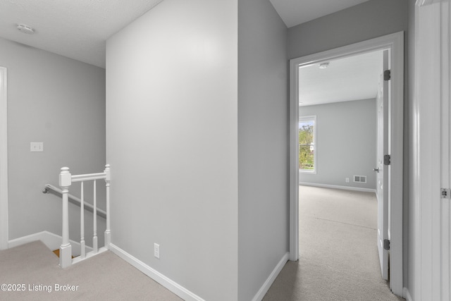 corridor featuring visible vents, carpet flooring, baseboards, and an upstairs landing