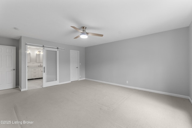 unfurnished bedroom with a barn door, light carpet, ensuite bathroom, and baseboards