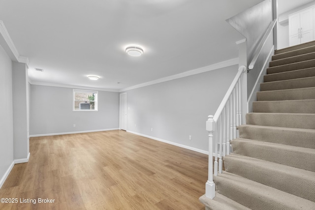 below grade area with light wood-type flooring, baseboards, stairway, and ornamental molding