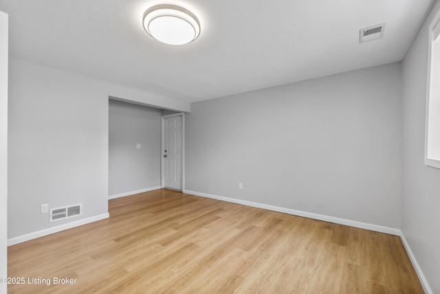 empty room with wood finished floors, visible vents, and baseboards