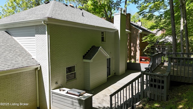 view of property exterior featuring a wooden deck, a chimney, a shingled roof, stairway, and brick siding