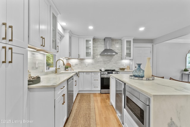 1907 Charbdin Pl, Louisville, KY 40207 - kitchen featuring appliances with stainless steel finishes, wall chimney exhaust hood, white cabinets, tasteful backsplash, and light wood-style flooring