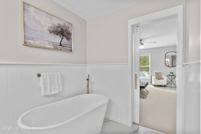 1907 Charbdin Pl, Louisville, KY 40207 - bathroom featuring a soaking tub, a wainscoted wall, marble finish flooring, ceiling fan, and a textured ceiling