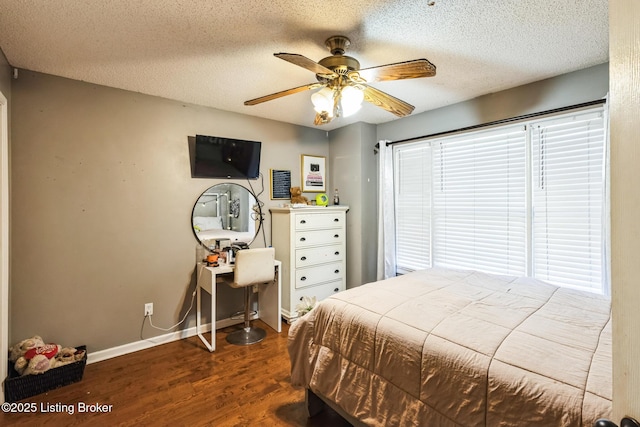 bedroom featuring a textured ceiling, ceiling fan, baseboards, dark wood finished floors, and multiple windows